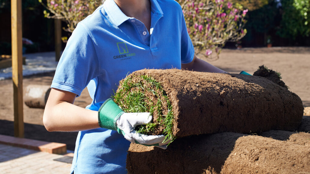 A landscaper works while wearing a polo shirt displaying the logo of her company. Custom branded apparel for landscaping companies. 