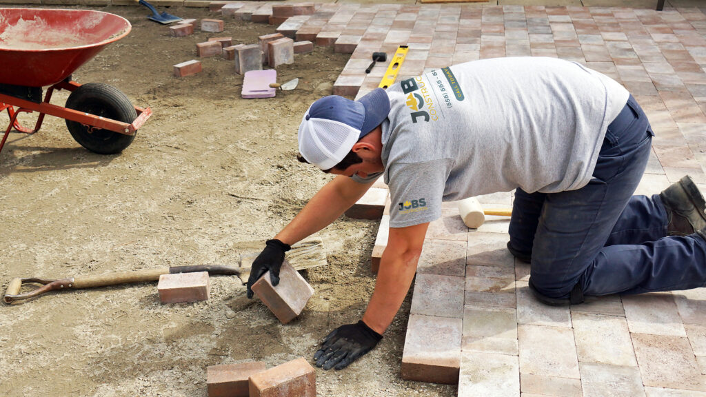 A man works on brick flooring while wearing a t-shirt branded with a construction company logo. Custom branded t-shirts for construction crews.