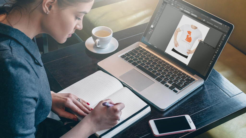 A woman is working on a t-shirt design for her custom merchandise order. 