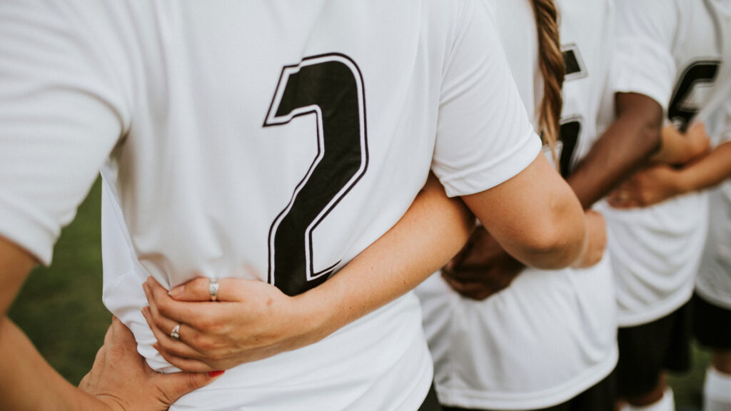 A group of three soccer players with their arms around each other. They are wearing white 100% polyester t-shirts. 