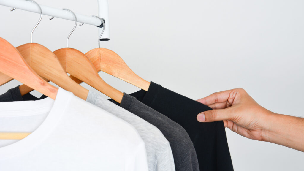 A person is picking out a t-shirt from a clothing rack filled with 100% cotton t-shirts for screen printing. 